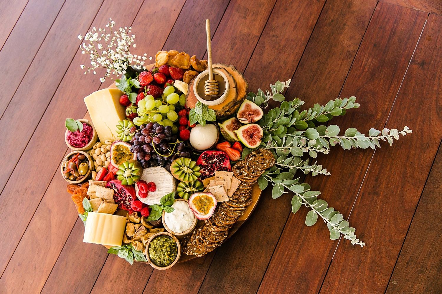 Artfully arranged grazing board with fresh fruits, bread, cheese and greenery on a dark wooden table surface.