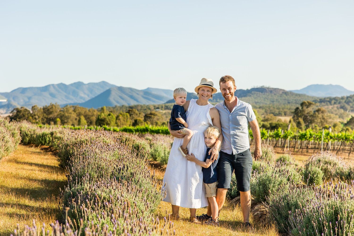 Family enjoying sunset at a scenic lavender farm with mountains and vineyards in the background.