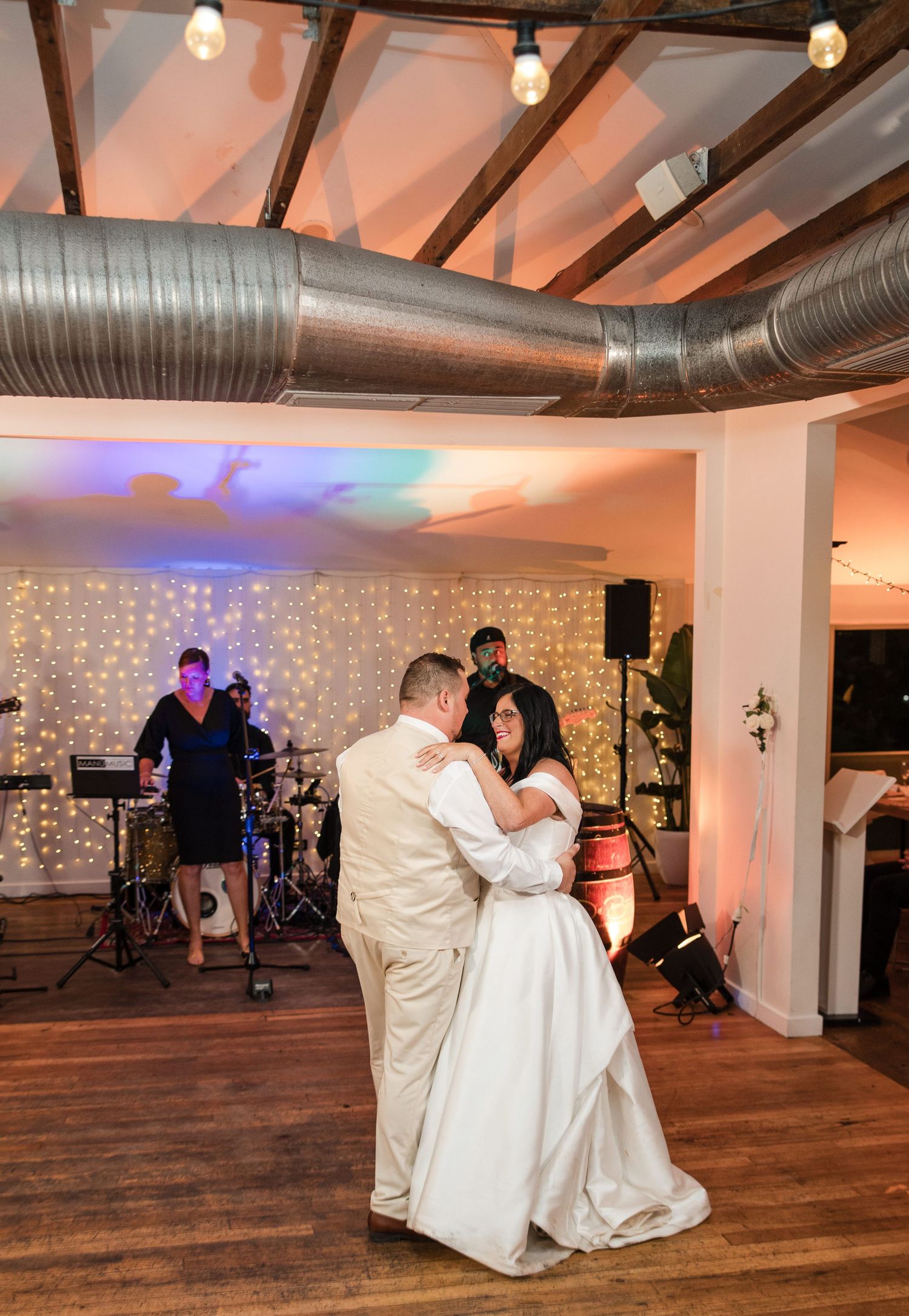 Bride and groom share first dance at wedding reception with live band performing on stage behind them.