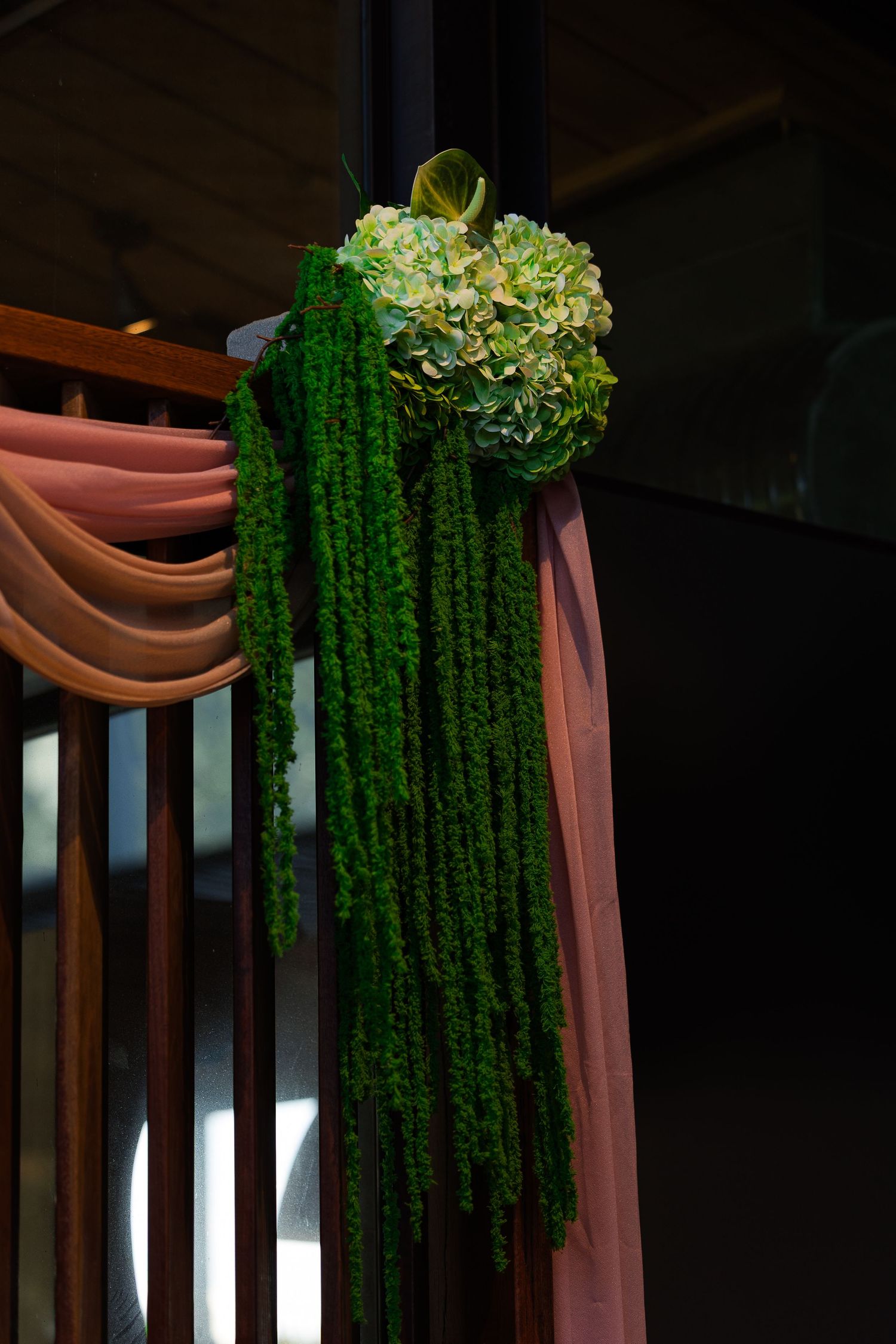 Green hydrangea and moss floral arrangement with pink fabric draping on wooden railing decor.