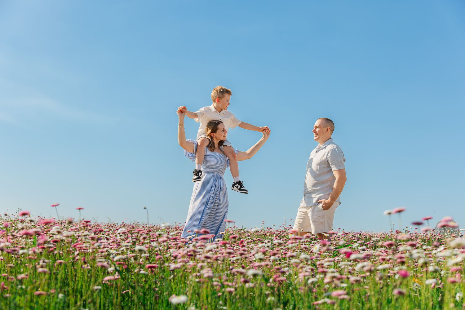 Family enjoying a sunny day in a blooming flower field under a clear blue sky.
