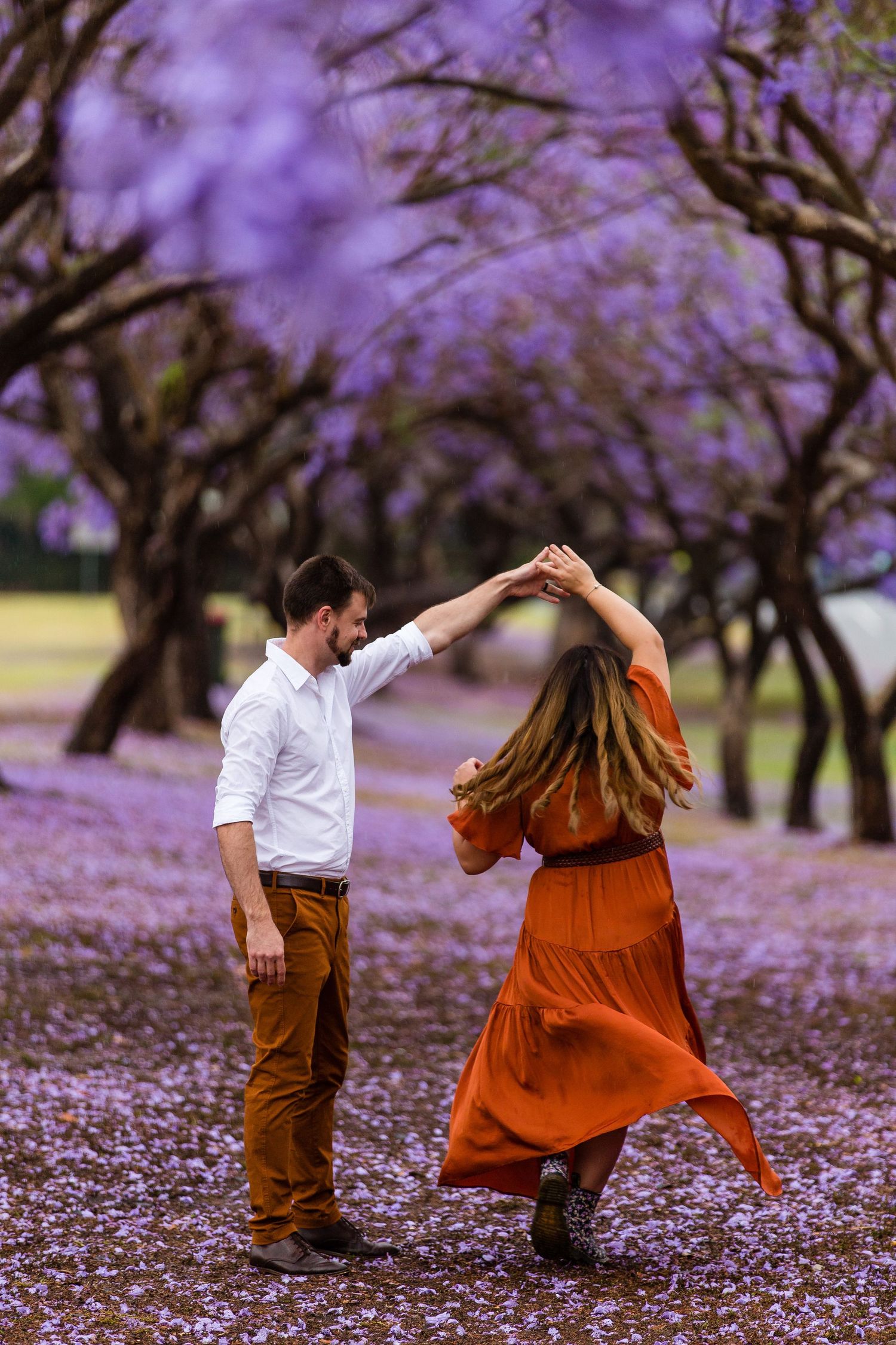 Couple dancing under blooming purple jacaranda trees with fallen petals covering the ground.