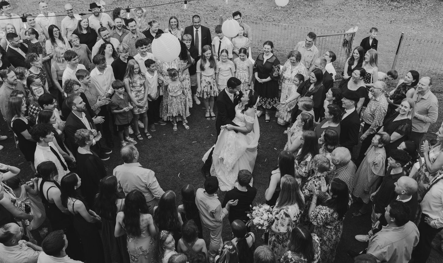 A black and white panoramic photograph shows a large crowd gathered outdoors for a social event or celebration.