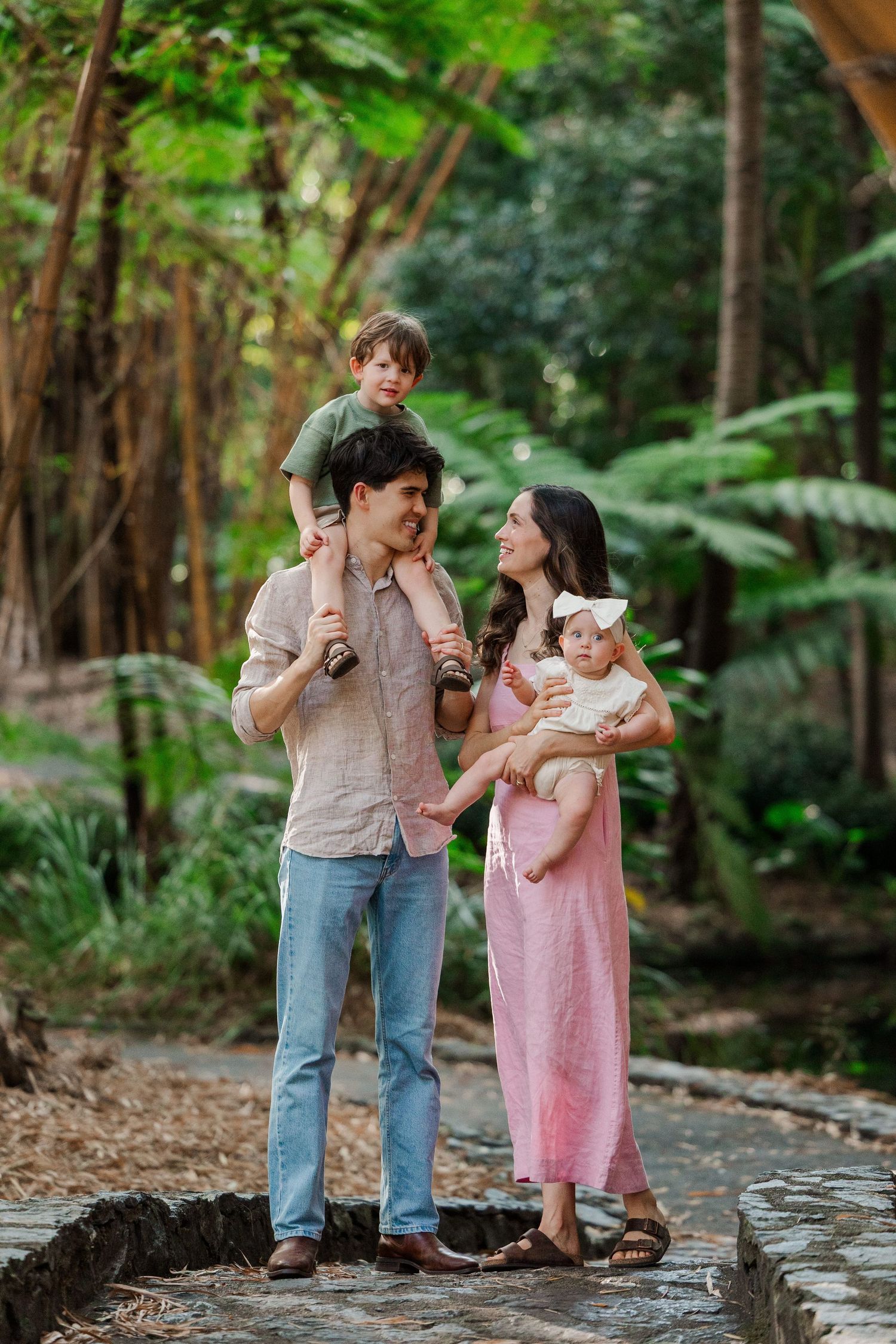 A couple shares tender moments with their baby in a lush forest setting while wearing casual attire.