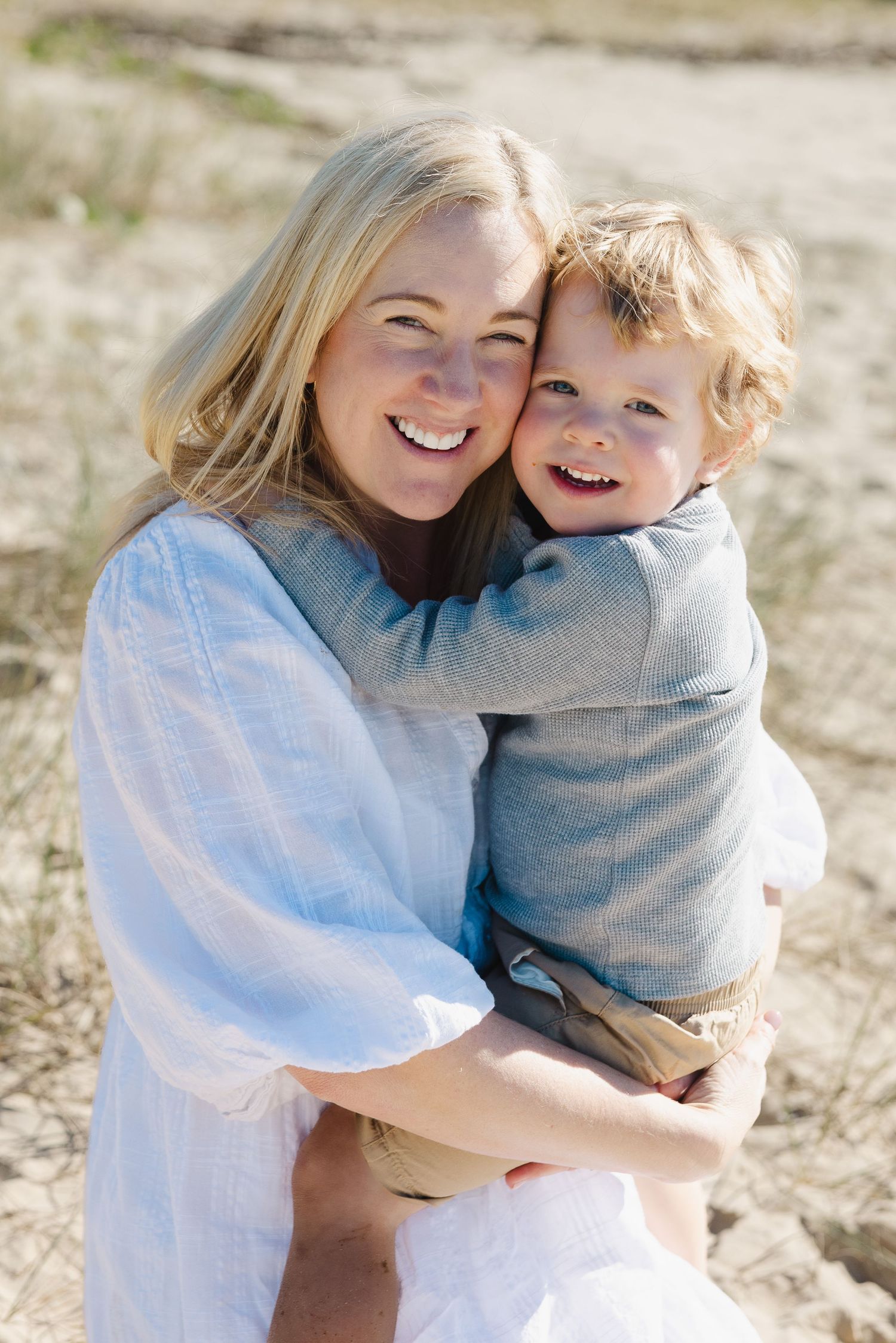Parent and child in matching grey sweaters share a joyful embrace outdoors in natural lighting.