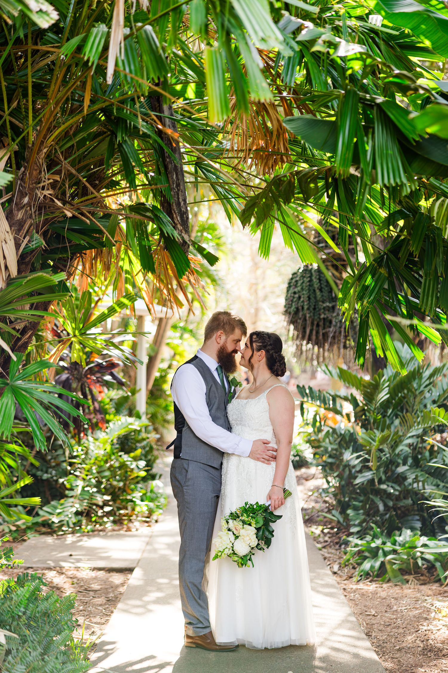 Bride and groom share a romantic moment surrounded by lush tropical greenery in a stunning outdoor garden wedding setting.
