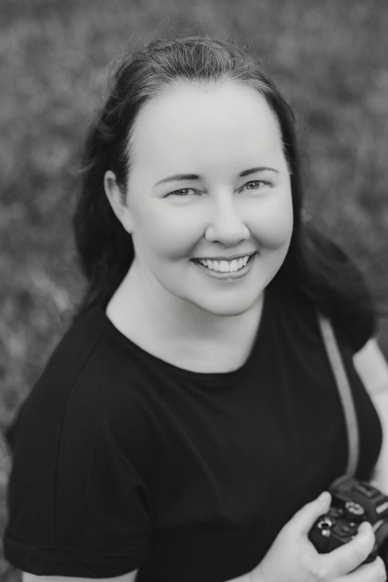 Black and white portrait photo of a smiling person in a black shirt holding something against a blurred background.