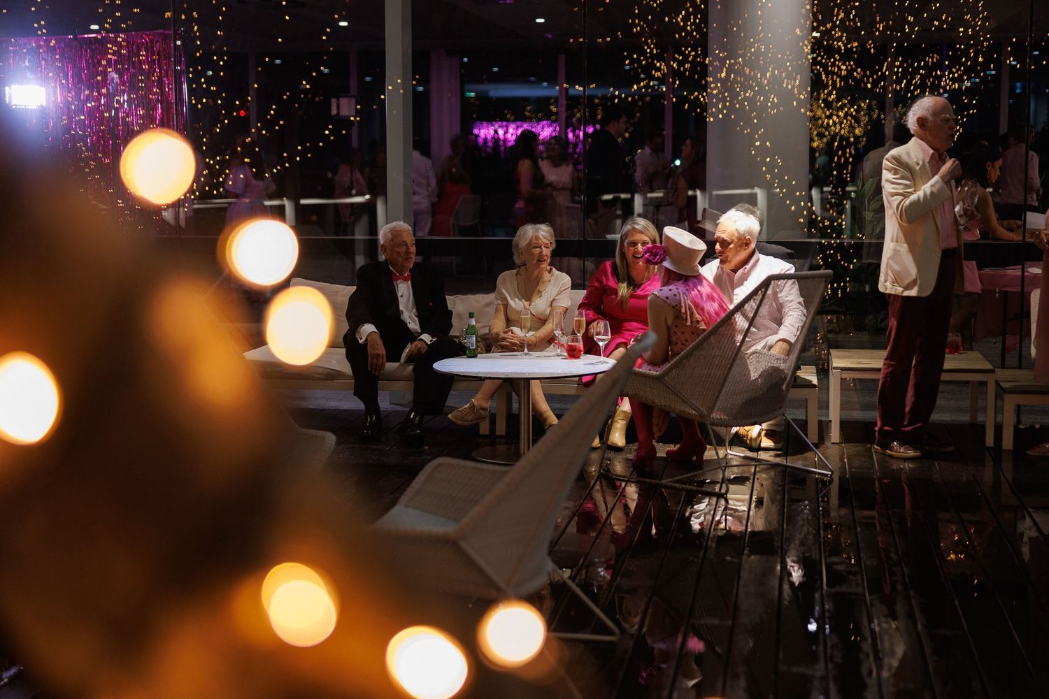 People gathered around a table in a dimly lit restaurant with soft bokeh lights and a festive evening atmosphere.