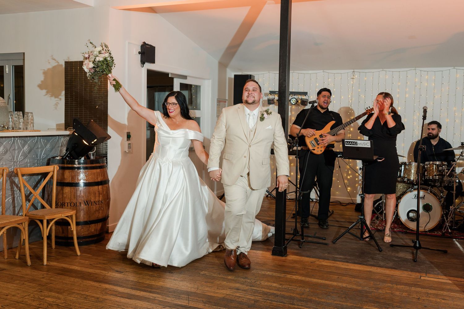 Bride and groom make grand entrance at wedding reception with live band performing in elegant white venue.