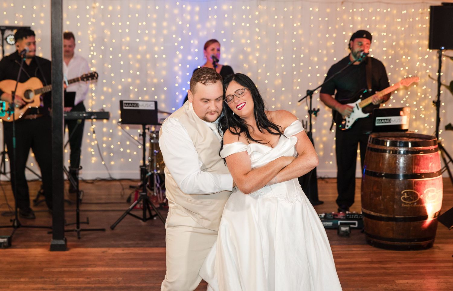 Bride and groom share a joyful first dance at wedding reception with live band performing on stage behind them.