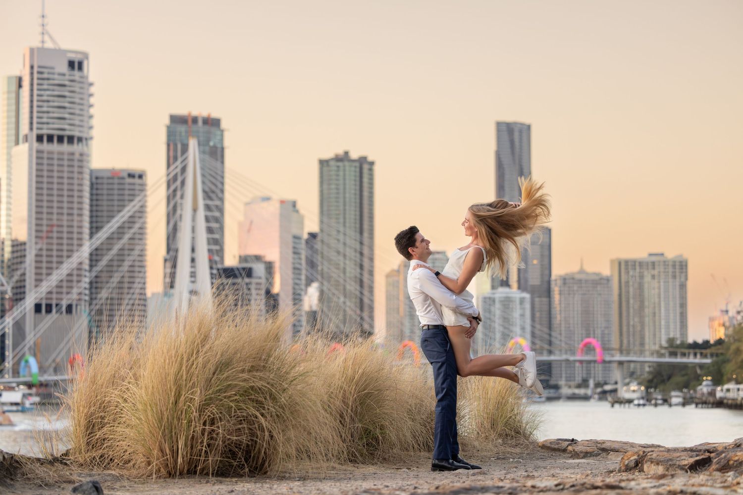 A couple shares a romantic dance pose against the Dubai skyline with tall skyscrapers and desert grass in the foreground.