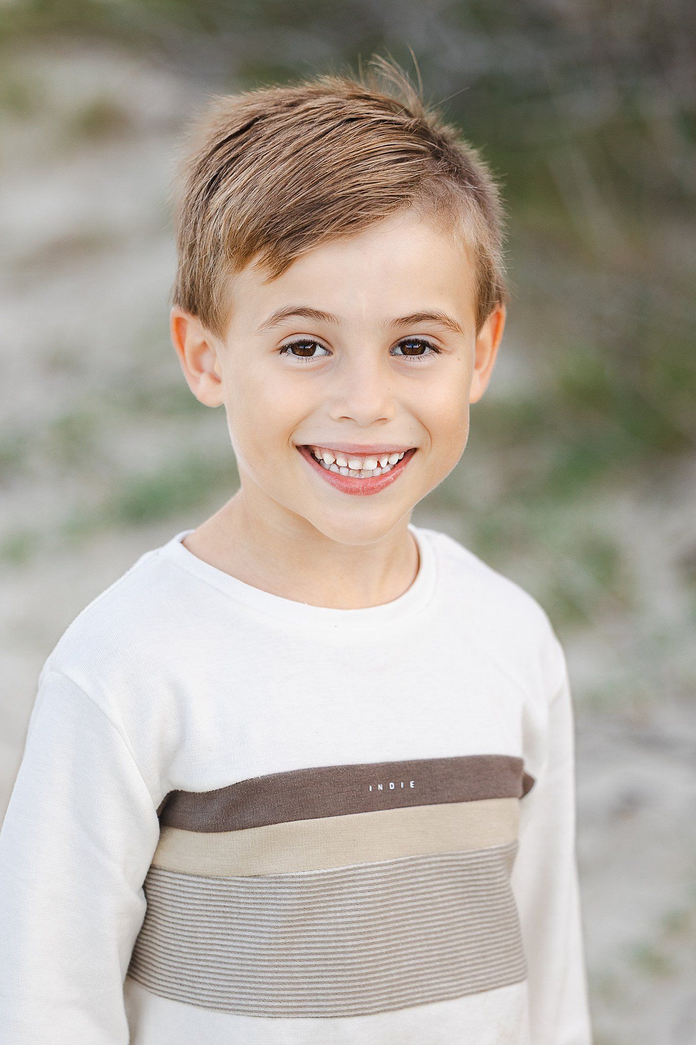 A cheerful child wearing a white sweater with brown and gray stripes smiles at the camera.