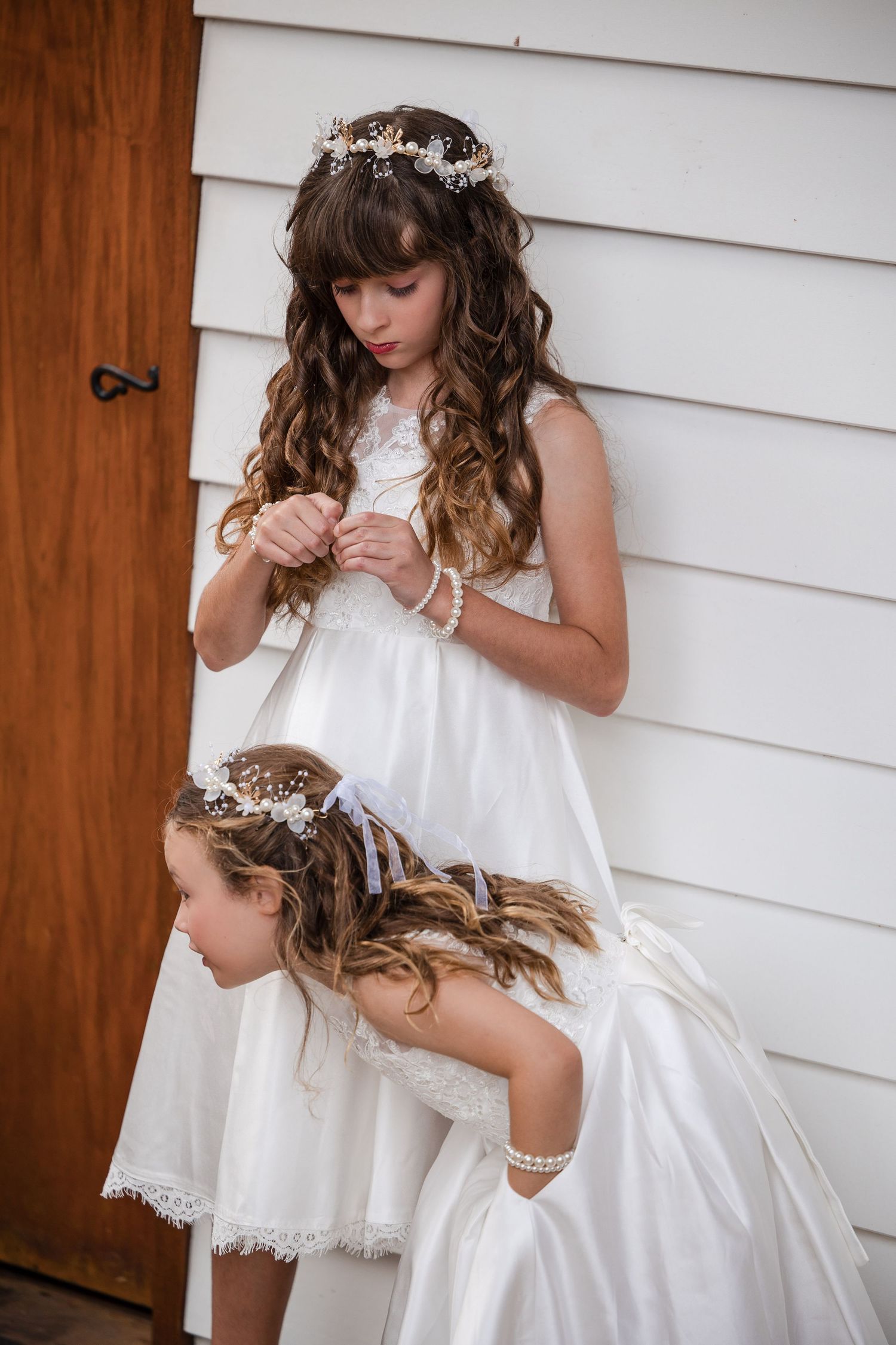 Two girls in white dresses and floral crowns pose outdoors, ideal for first communion or flower girl inspiration.