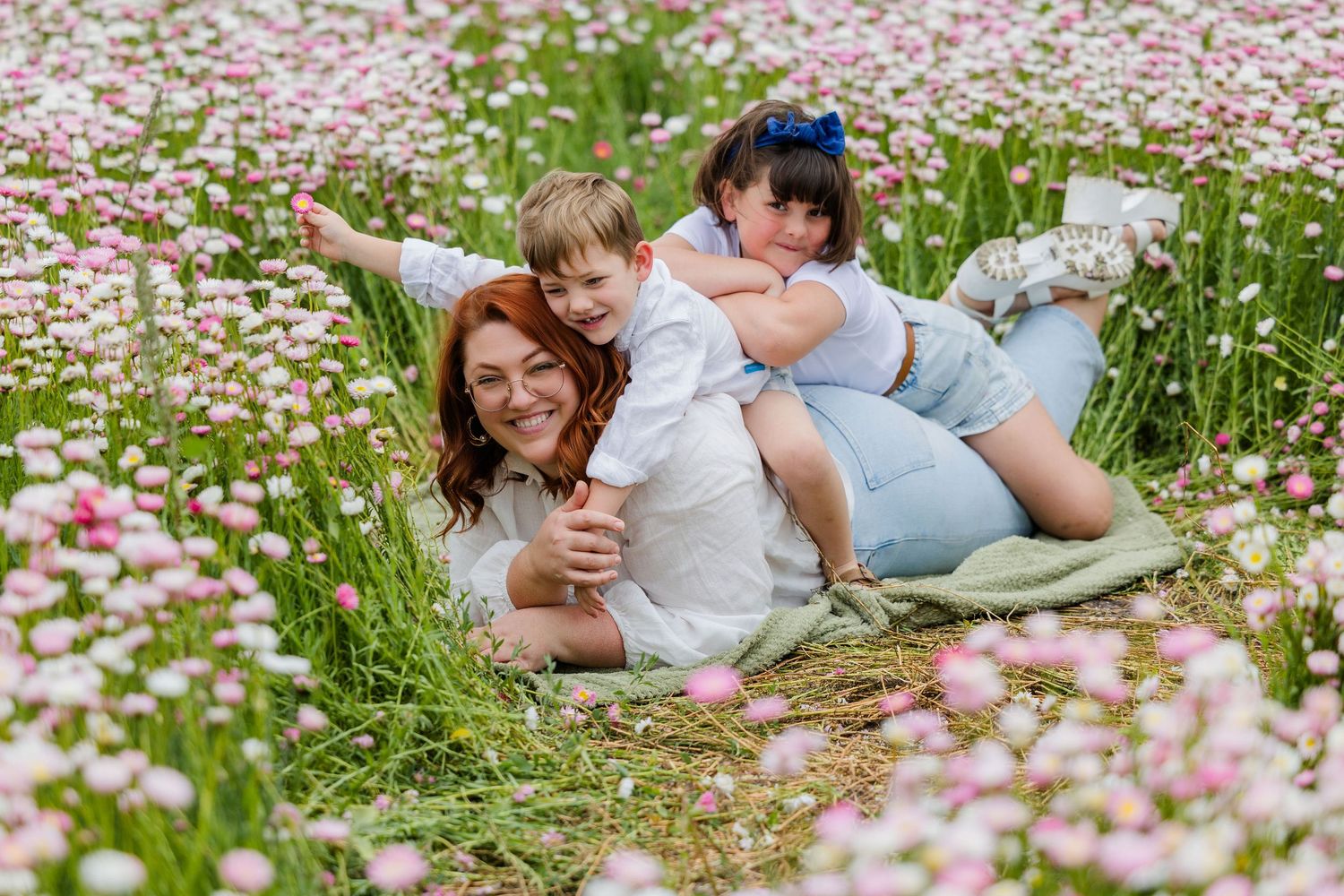 Couple lying together in a blooming meadow filled with pink and white daisies on a sunny summer day.