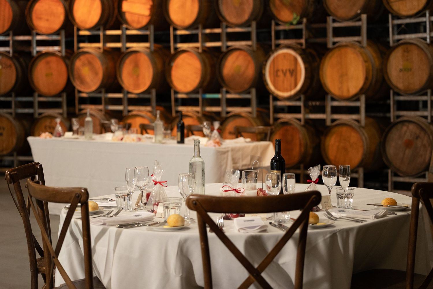 Elegant winery dining room with round tables set for dinner surrounded by oak wine barrels stacked along the walls.