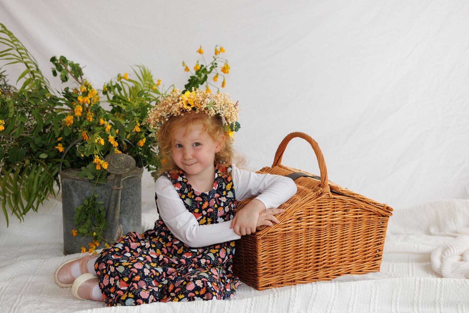 A child poses on a white floor near a wicker picnic basket with yellow sunflowers in the scene.