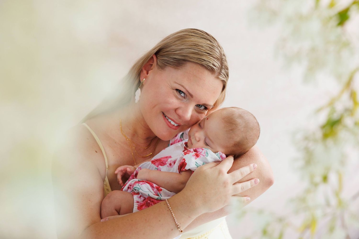 A smiling mother tenderly holds her newborn baby wrapped in a floral swaddle blanket.
