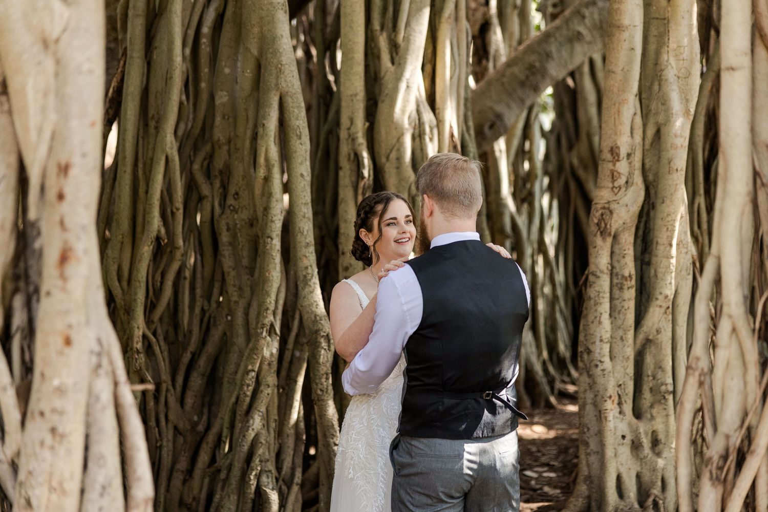 Bride and groom share a romantic moment surrounded by lush banyan tree trunks in an outdoor wedding photo.