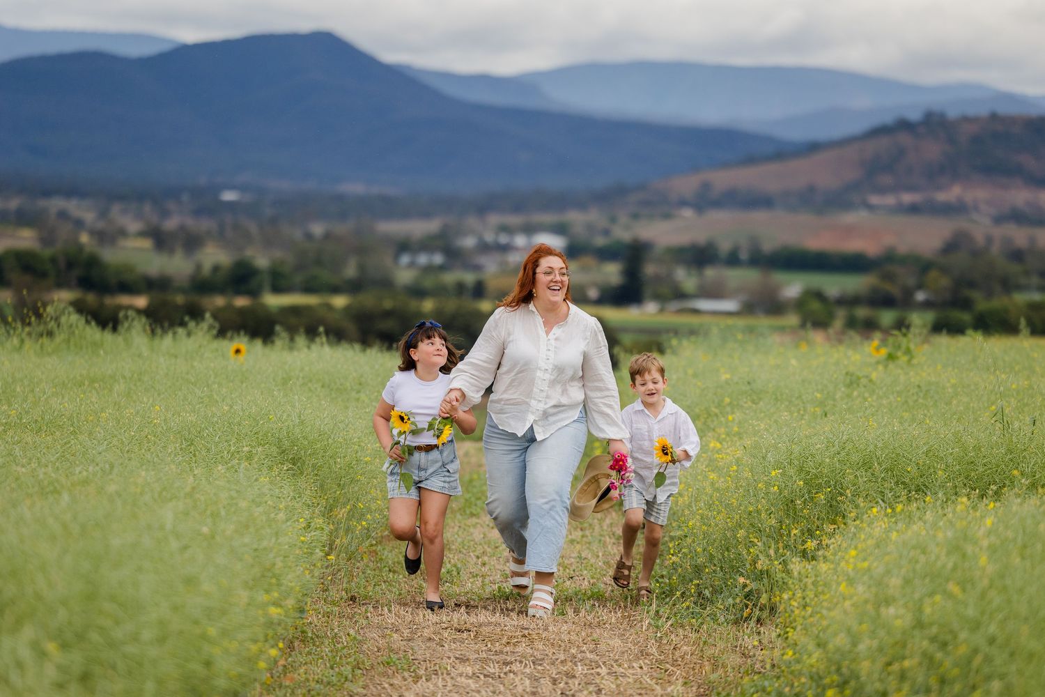 Woman and two children walk through a wildflower field with mountain views in the background.