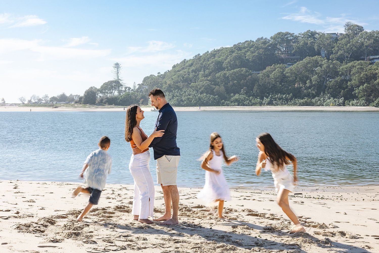 People enjoying a sunny day at the beach with mountains and lighthouse in the background.