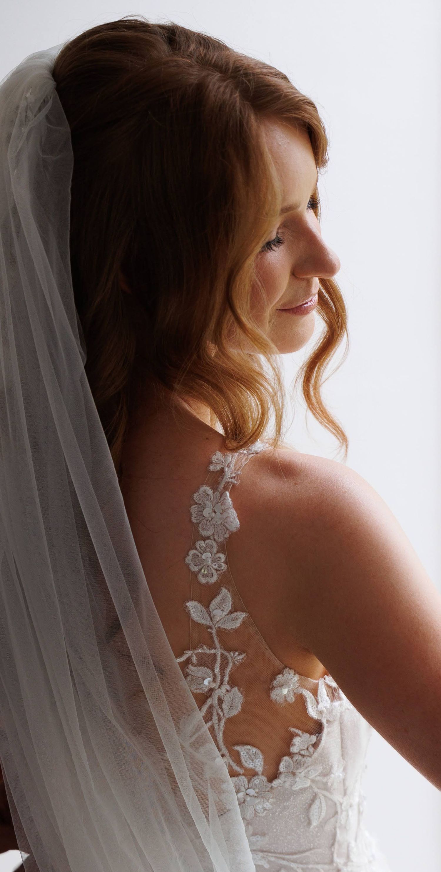 A wedding dress features intricate floral lace detailing and a flowing white veil.