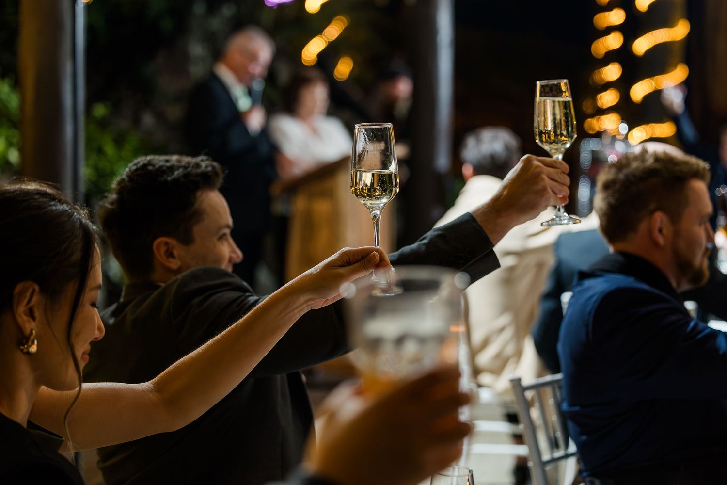Guests raising champagne glasses in a toast at an elegant evening celebration or wedding reception.