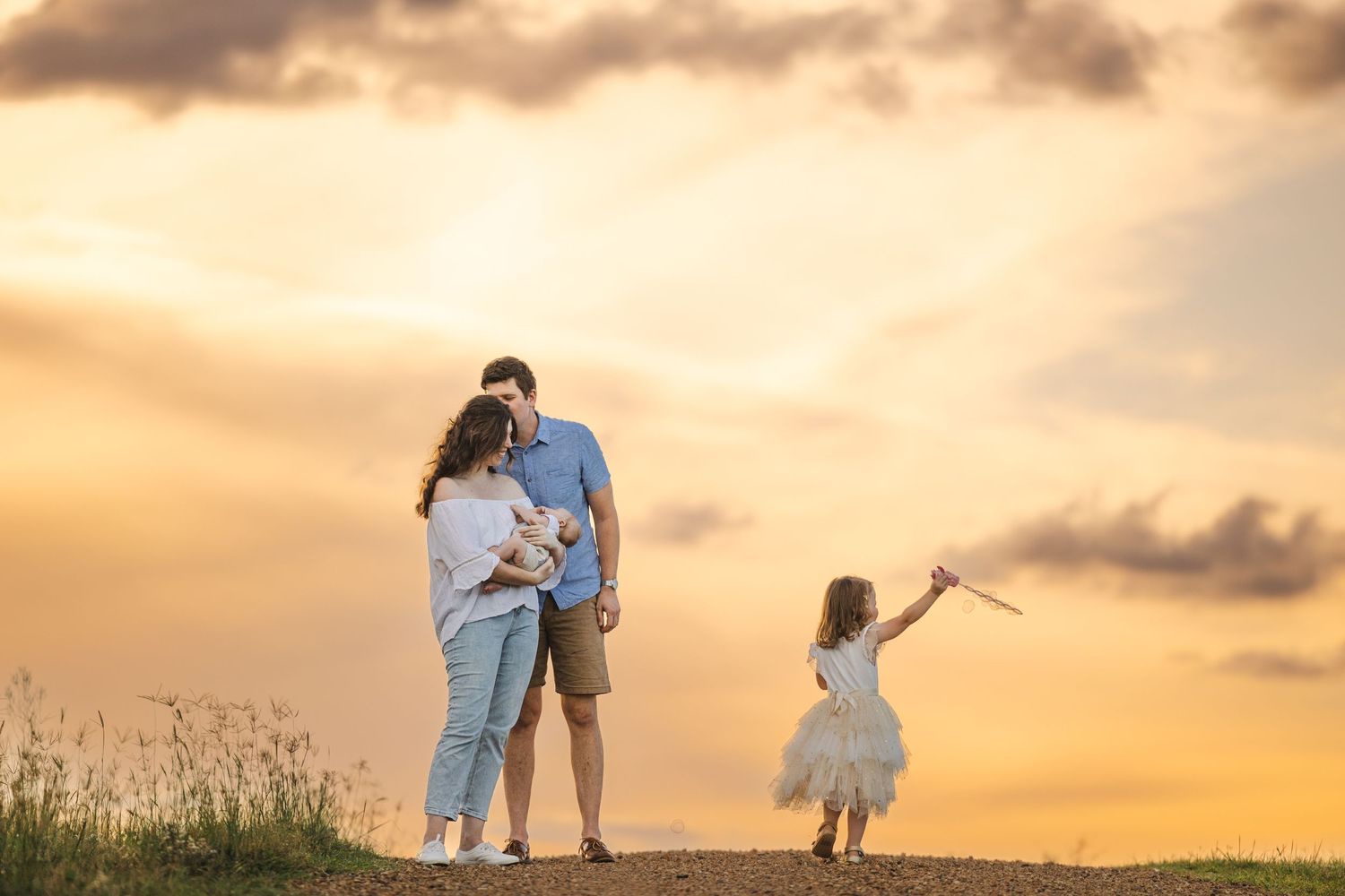 A silhouetted family stands on a hilltop against a golden sunset sky while a child dances joyfully.