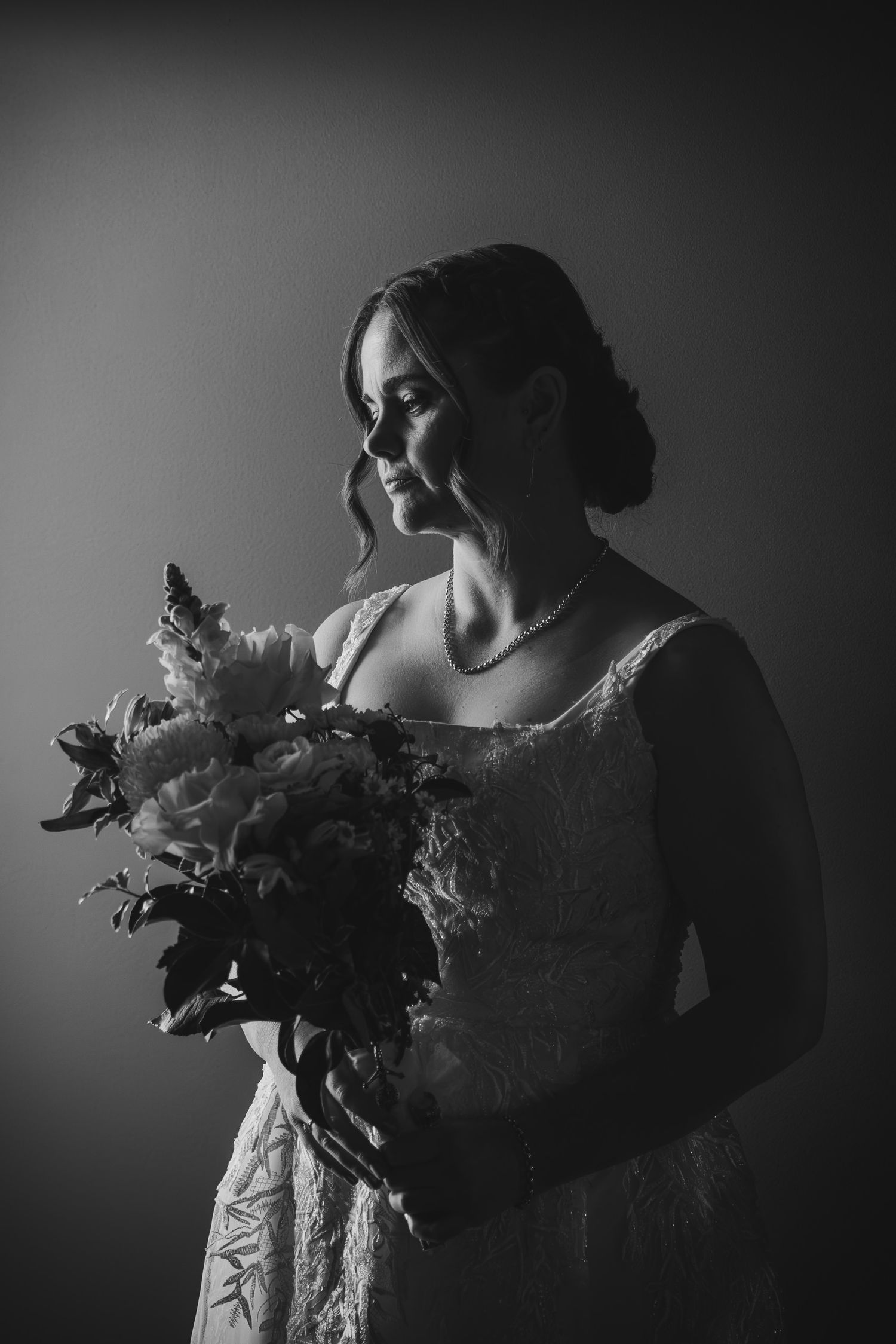 Black and white bridal portrait of a woman in lace gown holding a bouquet, soft studio lighting.