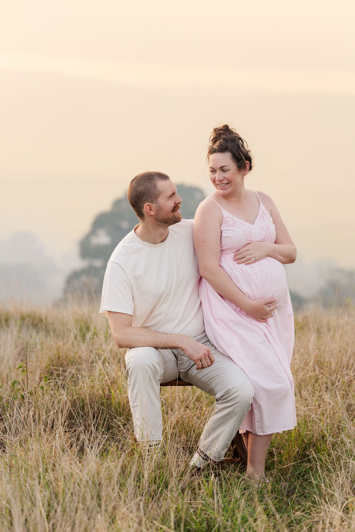 A couple sits together in a golden field during sunset sharing intimate moments in a four-part photo series.