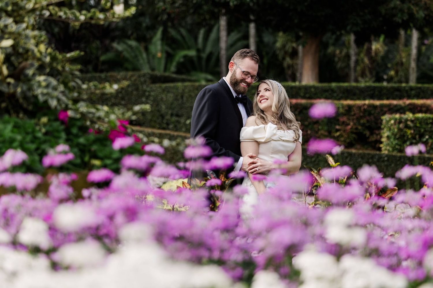 A couple shares a romantic moment in a garden with vibrant purple flowers blooming in the foreground.
