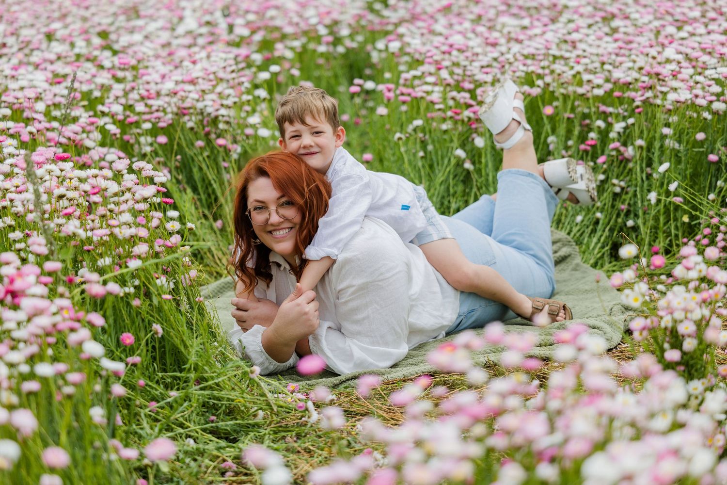 A couple relaxes in a meadow filled with pink cosmos flowers on a sunny summer day.
