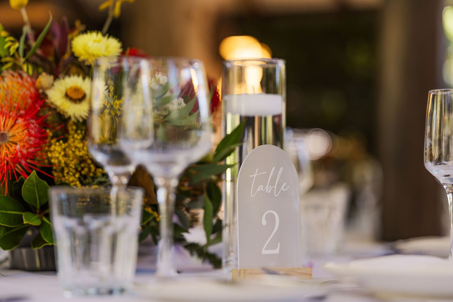 Elegant wedding table setting with floral centerpiece, wine glasses, and a Table 2 sign at a reception.