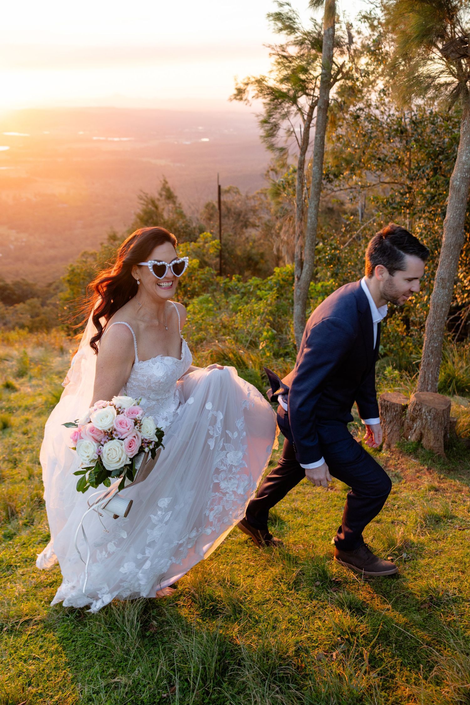 A couple shares a romantic moment at sunset on a hilltop surrounded by trees and golden light.