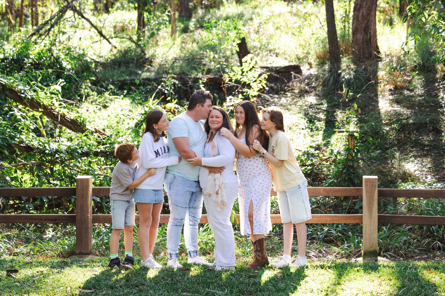 A group in white outfits walks together along a wooden fence path through a lush green garden setting.
