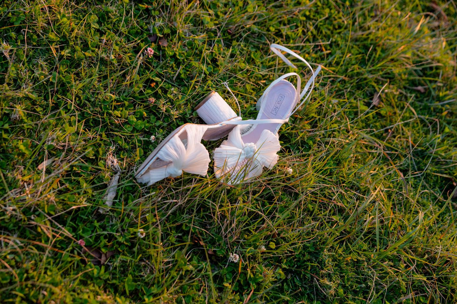 A pair of white sneakers lying in green grass illuminated by sunlight.