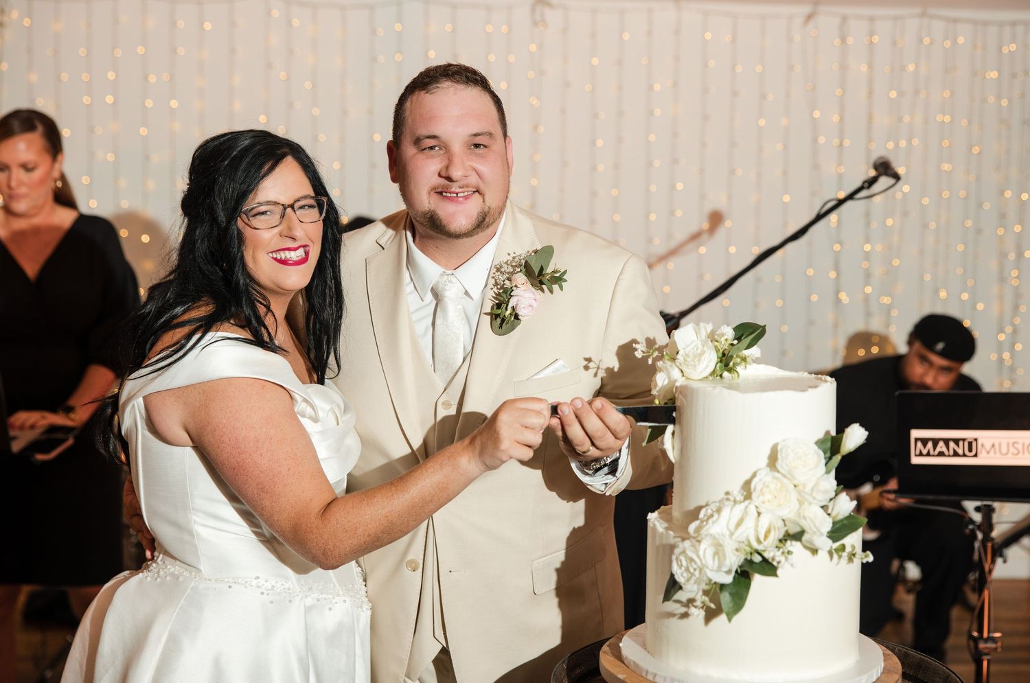Bride and groom smiling while cutting their white tiered wedding cake at their elegant reception.