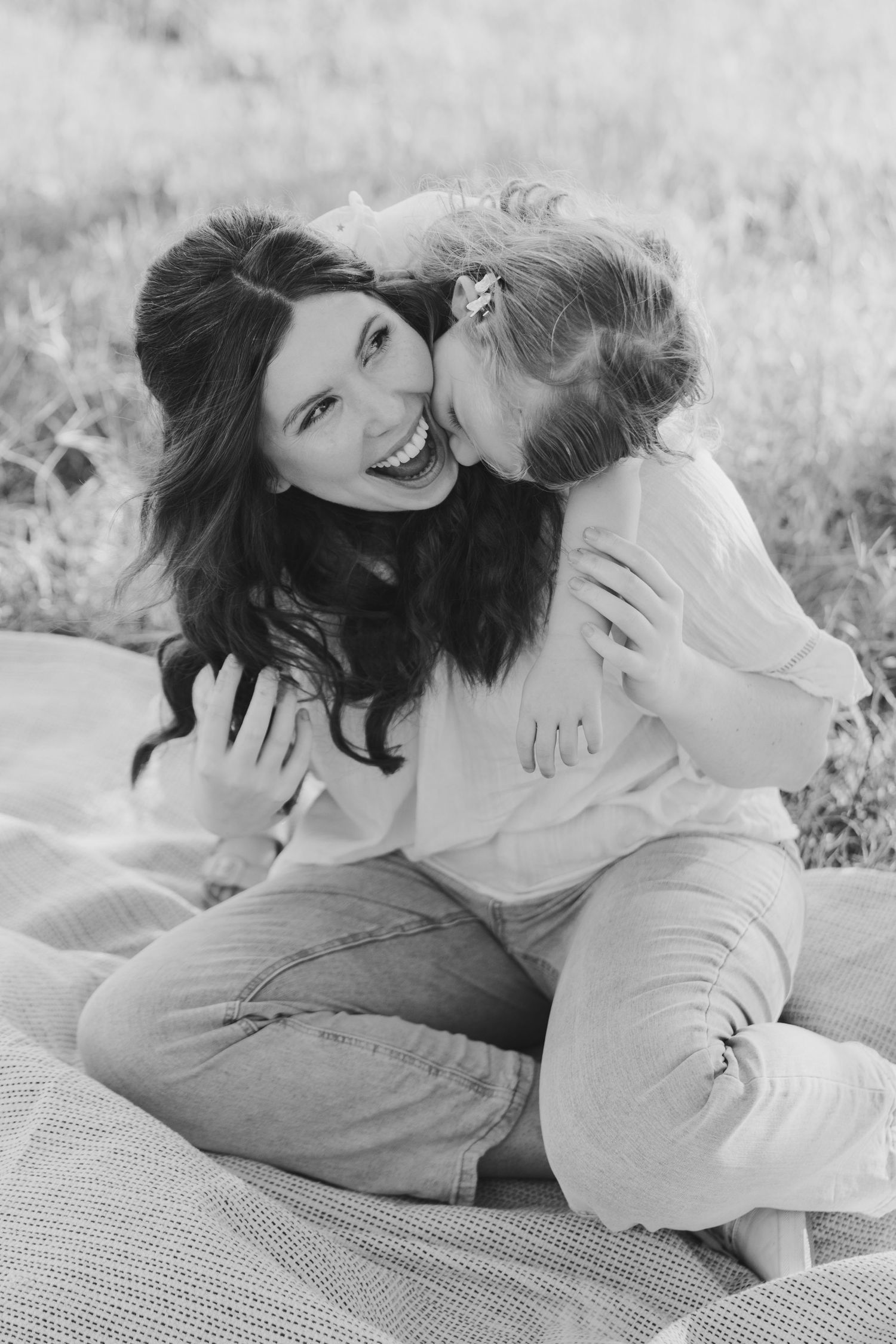 A joyful black and white portrait of parent and child sharing an affectionate moment on a blanket outdoors.