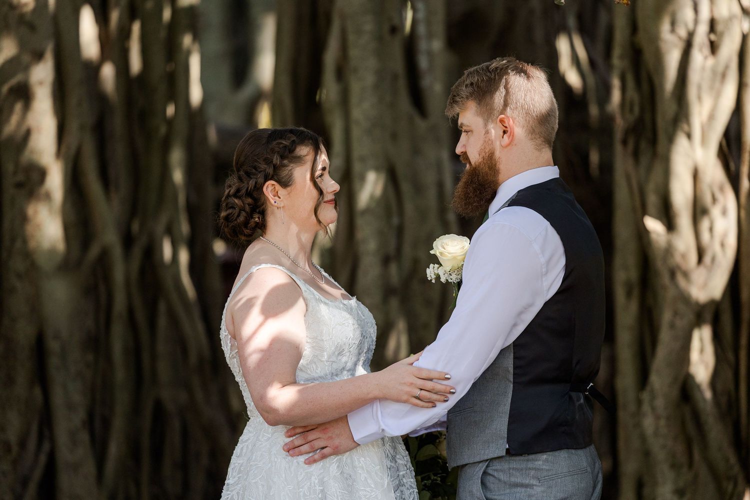 Bride and groom share a tender moment holding each other in front of large banyan trees on their wedding day.