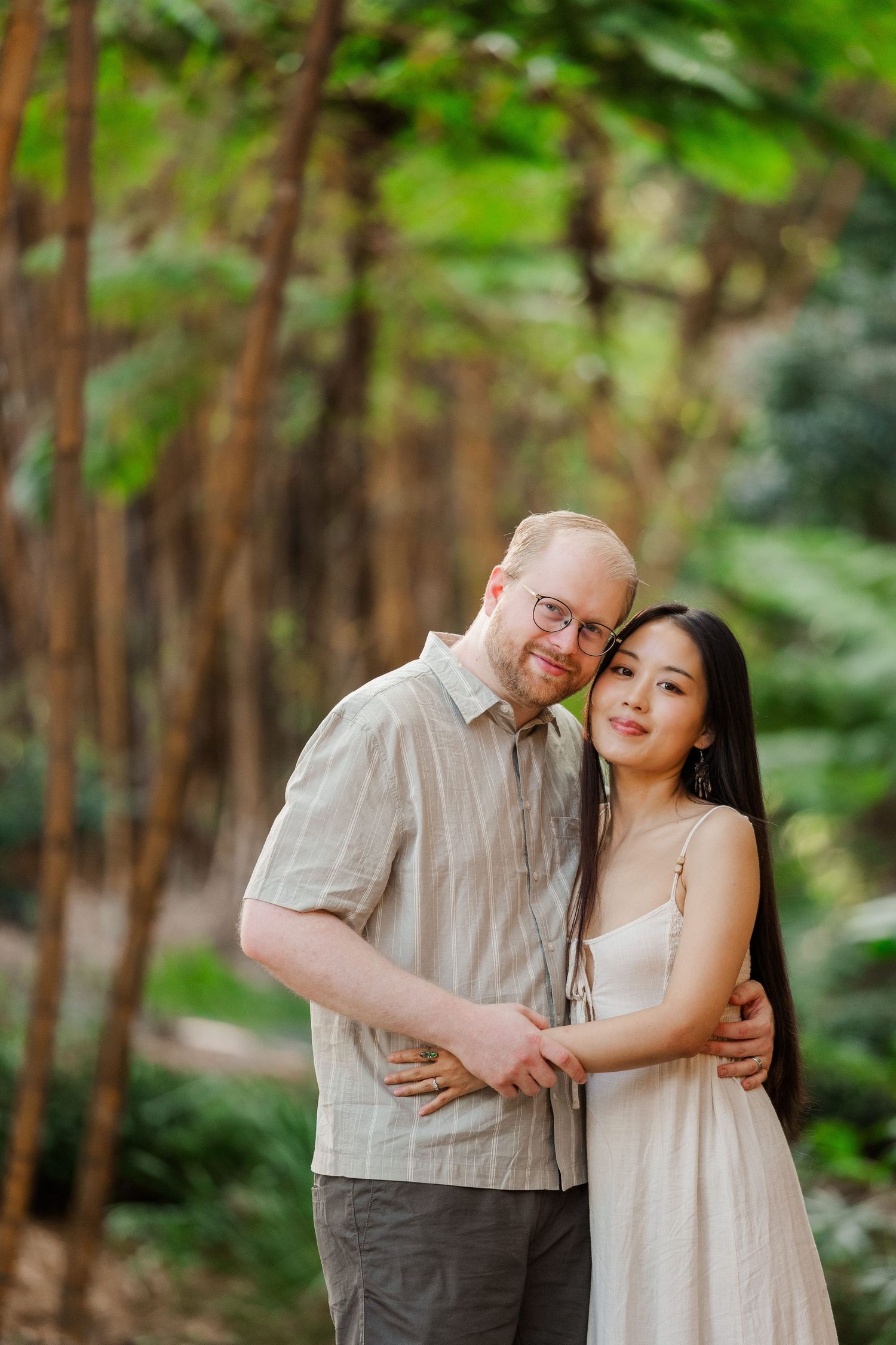 A couple embraces while standing in a serene bamboo forest setting with soft natural lighting.