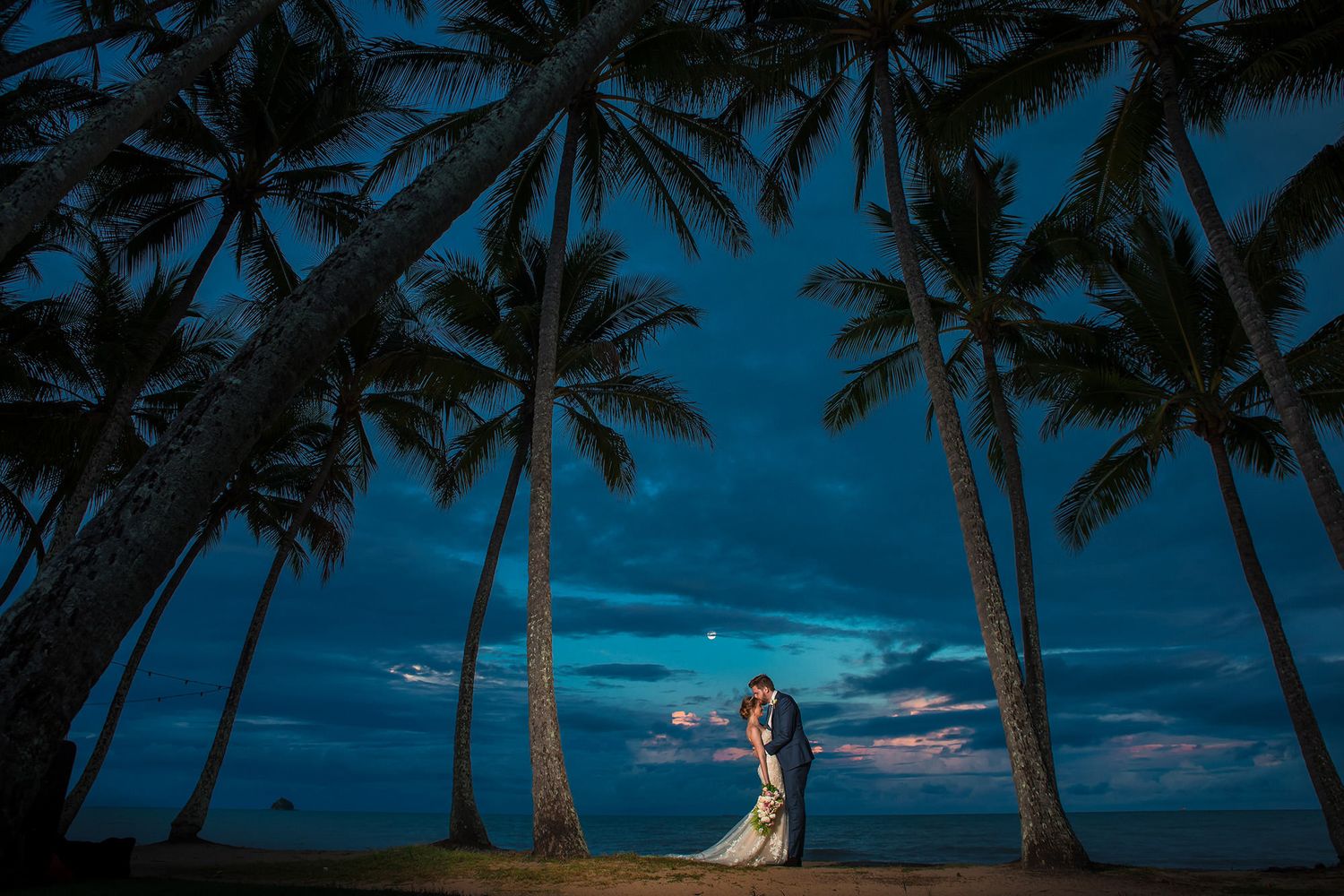 Romantic twilight wedding portrait under palm trees on a tropical beach.