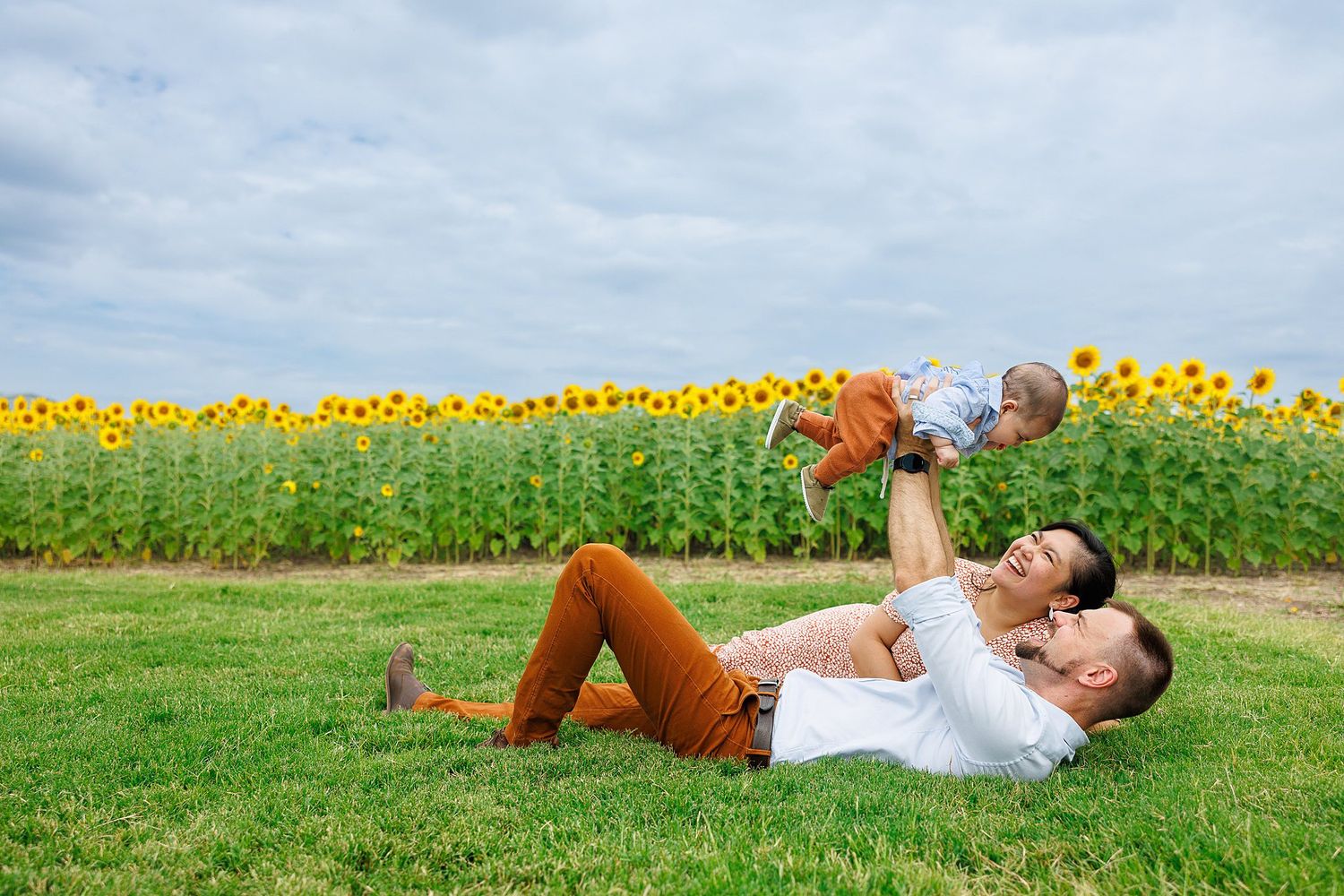 Two people enjoying a summer day lying on grass near a vibrant field of blooming sunflowers.