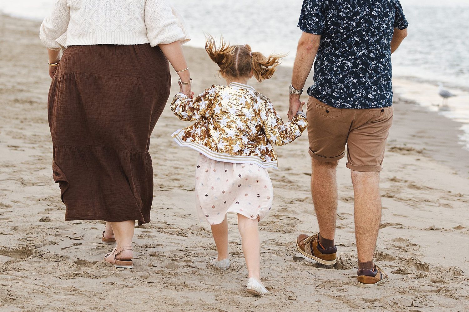 Family holding hands and walking together barefoot on a sandy beach during a summer day.