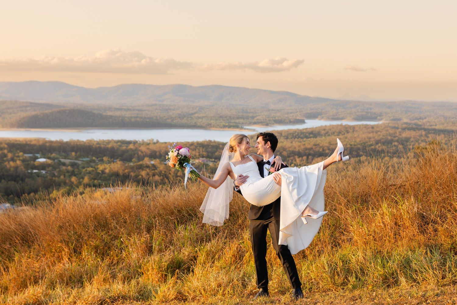 A couple shares romantic moments in a golden field at sunset with mountains in the background.