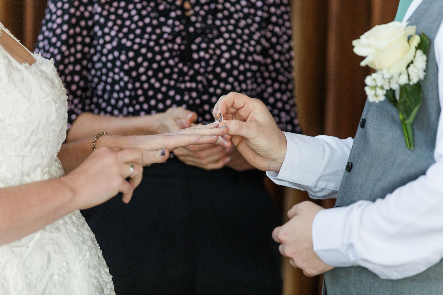 Bride and groom exchanging wedding rings during ceremony with officiant in background.