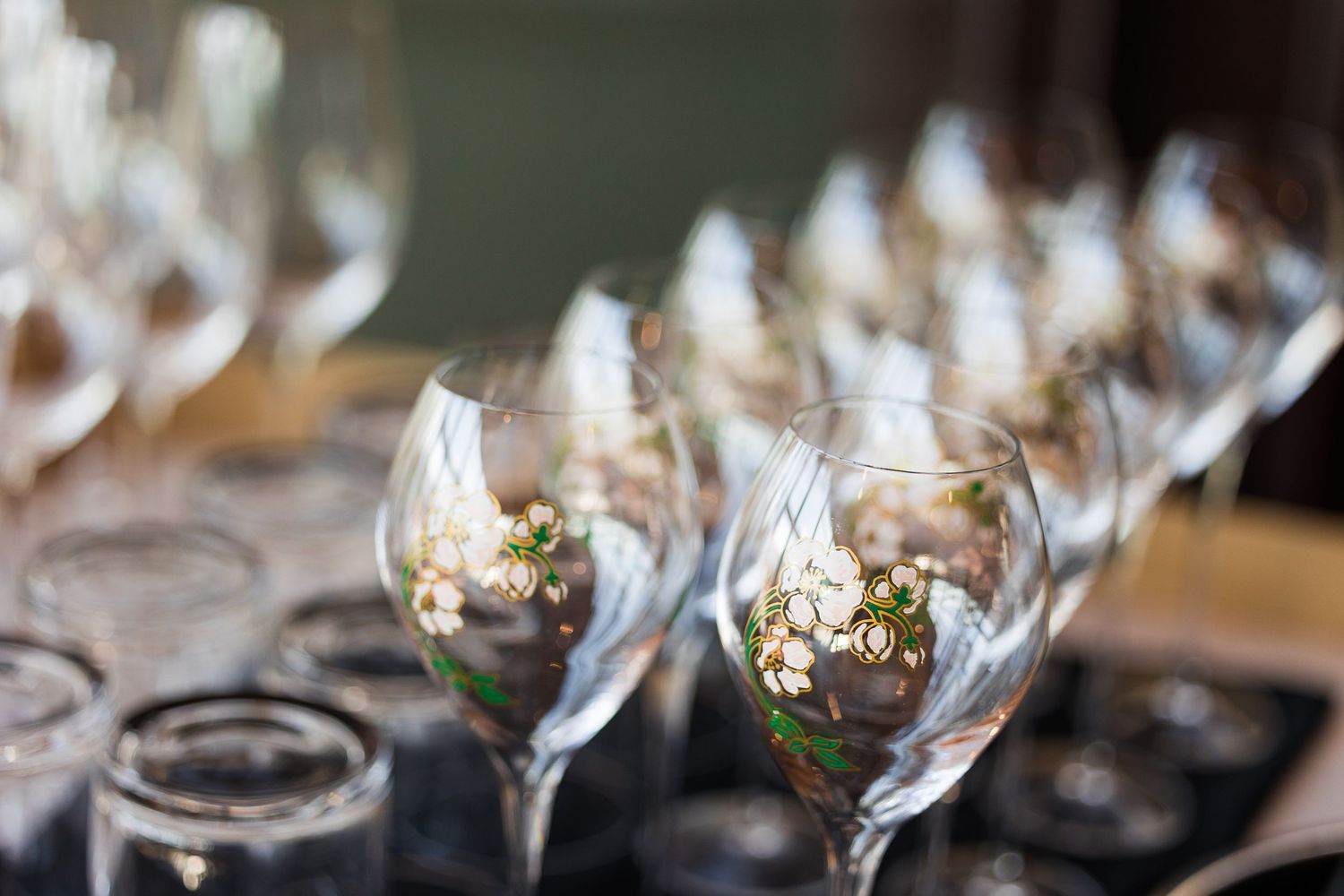 Elegant wine glasses with delicate floral arrangements displayed on a dark tray at a wedding reception.