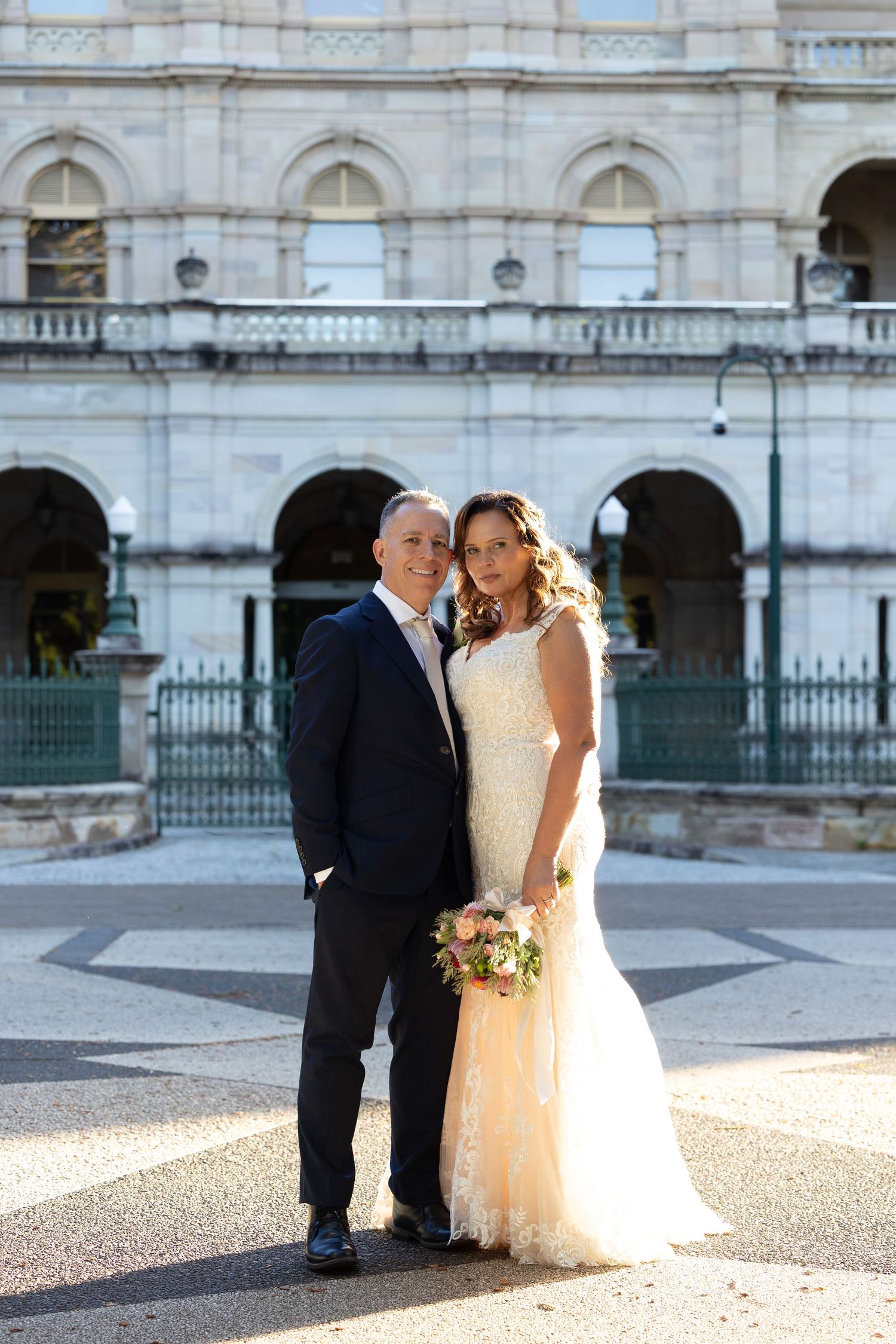 A romantic wedding couple shares intimate moments in front of a grand historic building facade.