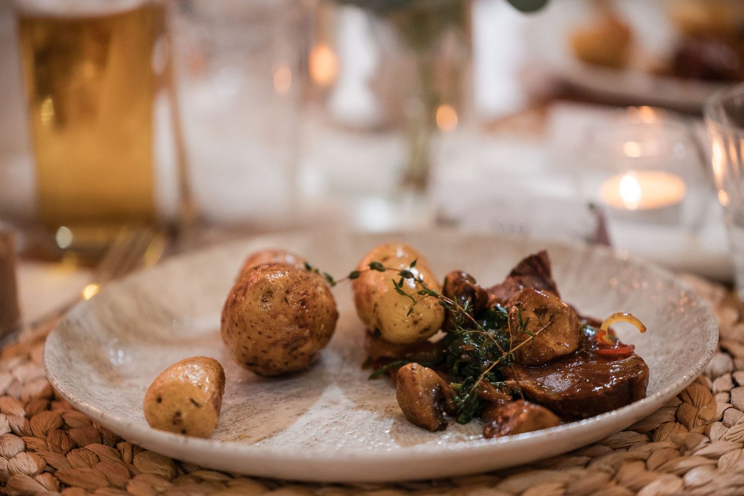 Roasted potatoes and glazed meat garnished with fresh herbs served on a white plate at an elegant dinner table.