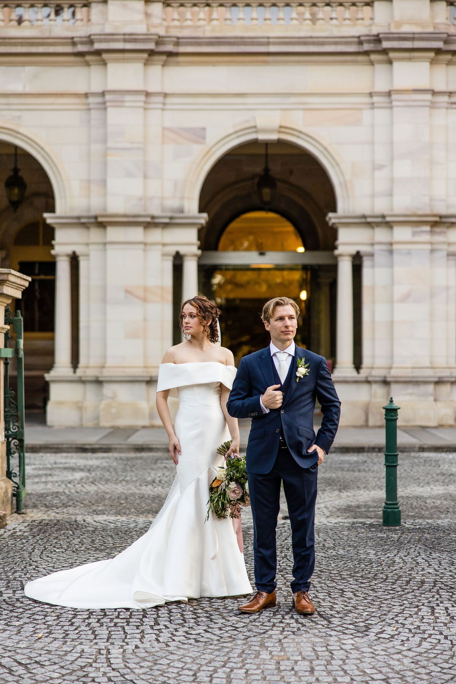 An elegant wedding portrait in front of a classical stone building with arched columns.