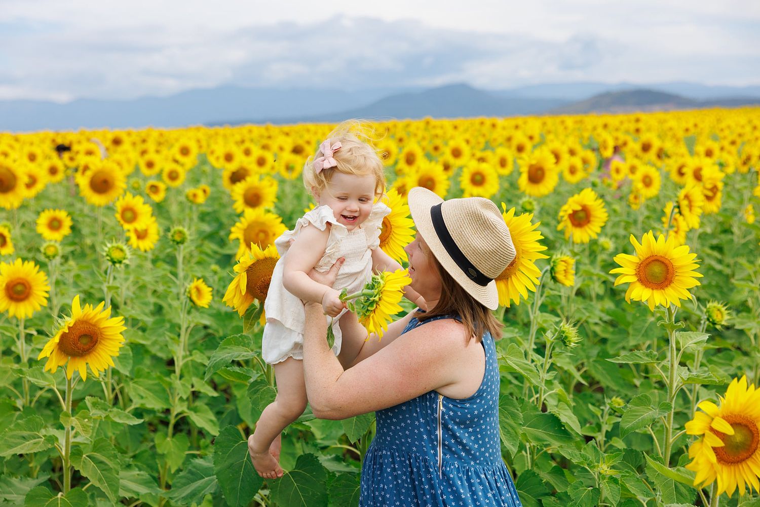 A pair enjoying a tender moment together in a bright yellow sunflower field under cloudy skies.