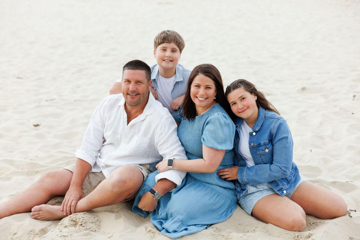 Group of people wearing coordinating blue and white outfits sitting and laying on a sandy beach.